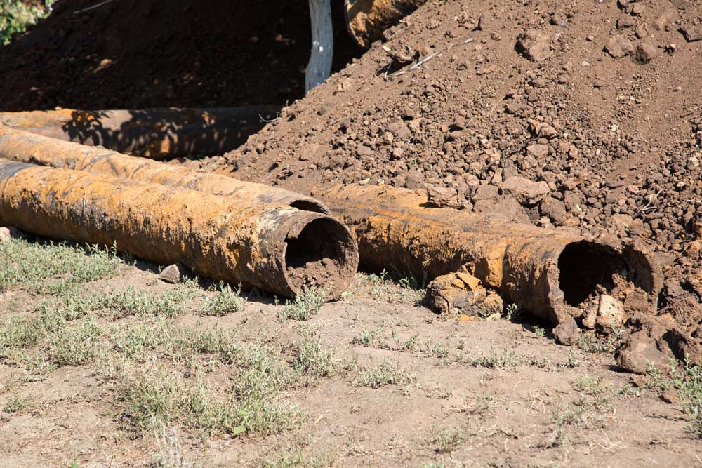 Rusty underground pipe exposed in a dirt trench