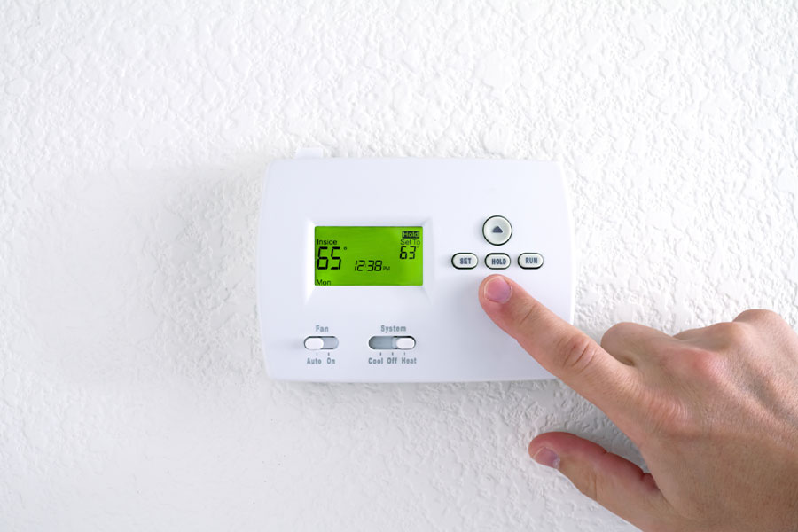 Person adjusting a digital thermostat on the wall