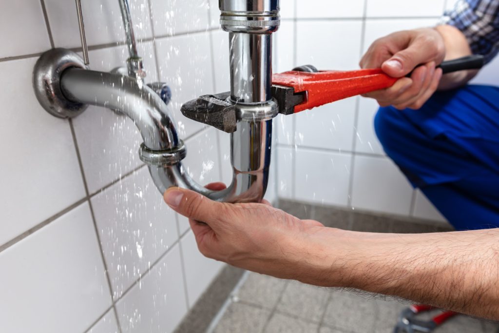 Plumber fixing a leaking pipe under a sink with a wrench