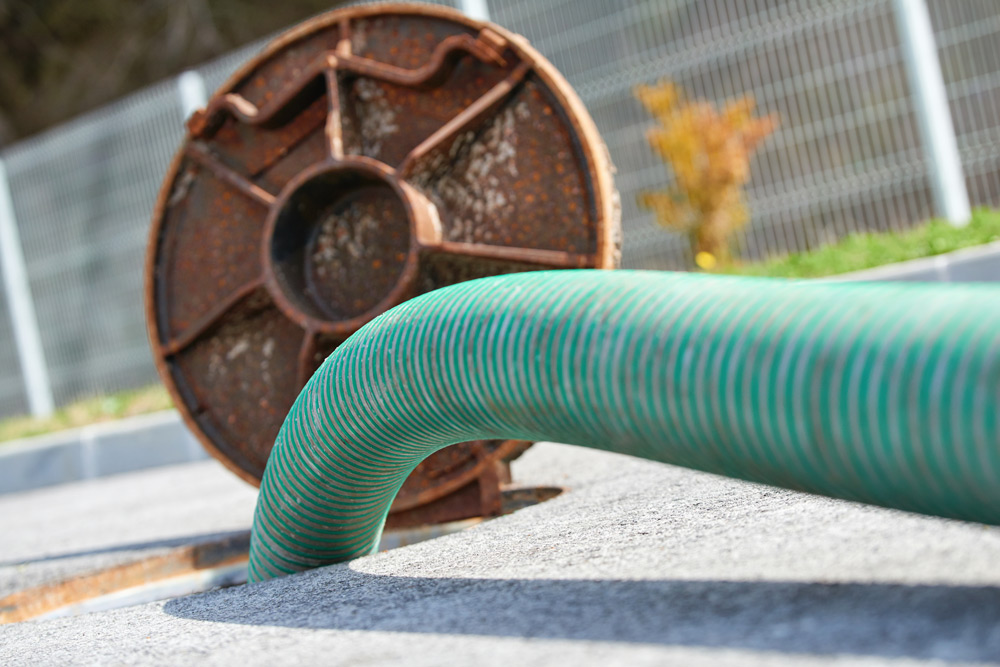 Green hose connected to an open manhole with a rusted cover nearby