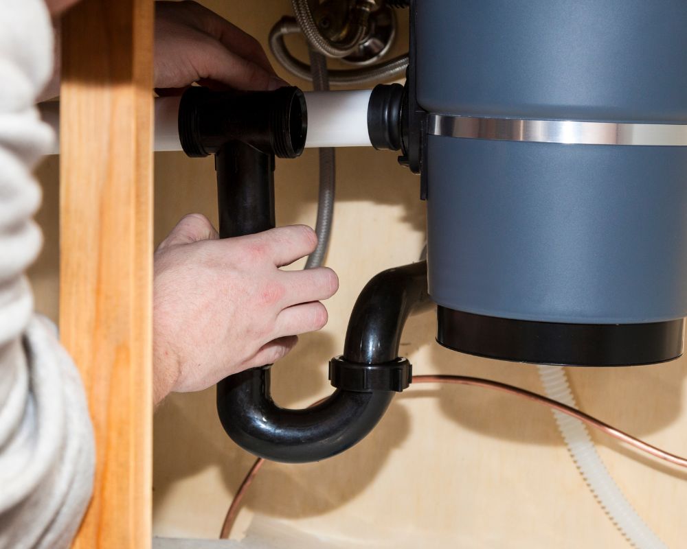 Technician connecting plumbing pipes to a kitchen sink disposal unit